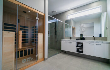 Modern ensuite bathroom featuring a built-in wooden sauna cabana, glass walk-in shower, double vanity, and large wall mirror.