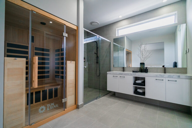 Modern ensuite bathroom featuring a built-in wooden sauna cabana, glass walk-in shower, double vanity, and large wall mirror.