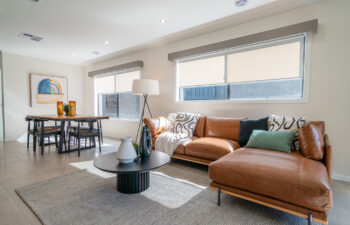Open-plan living space featuring a brown cognac leather sectional sofa, round black coffee table, textured rug, and a dining area in the background.