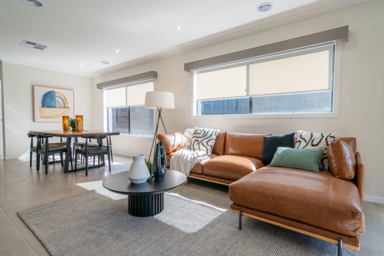 Open-plan living space featuring a brown cognac leather sectional sofa, round black coffee table, textured rug, and a dining area in the background.