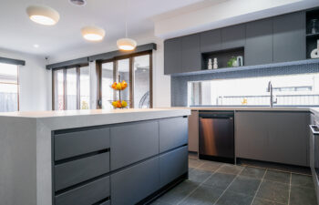 Modern kitchen featuring a waterfall island bench with charcoal cabinetry, dark grey tile floor, black mosaic backsplash, and pendant lighting.