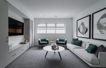 Modern media room featuring a light grey sofa, dark teal velvet armchairs, dark grey carpet, built-in TV unit, and large abstract wall art.