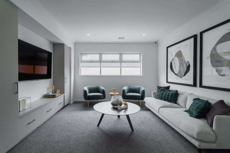 Modern media room featuring a light grey sofa, dark teal velvet armchairs, dark grey carpet, built-in TV unit, and large abstract wall art.