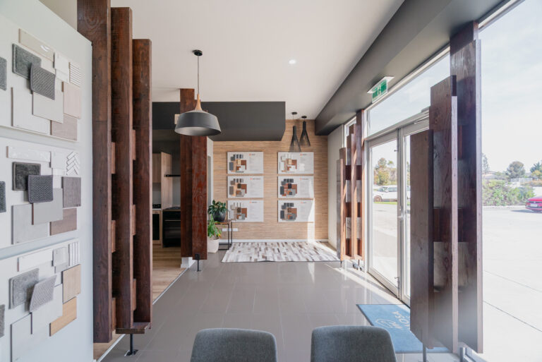 Modern interior design studio showroom featuring material sample boards, dark timber posts, tile flooring, and glass entry doors.