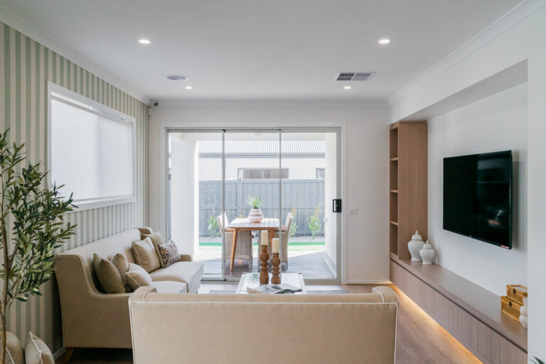 Cozy living room with beige sofas, a striped feature wall, a wall-mounted TV, and sliding glass doors opening to an outdoor patio dining area.