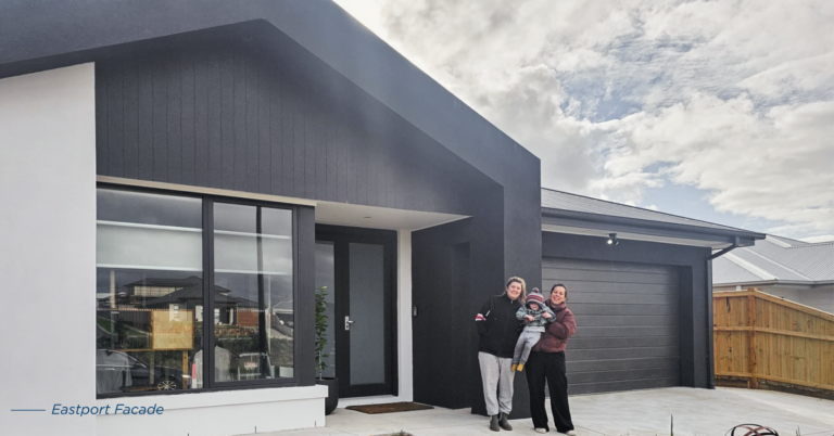 A family standing outside a modern single-story house with black trim, a garage, and a white interior doorway.